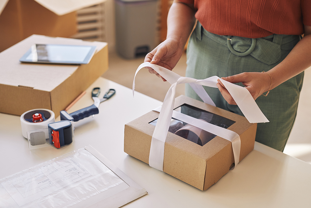 close up woman decorating cardboard box with ribbon table before delivery